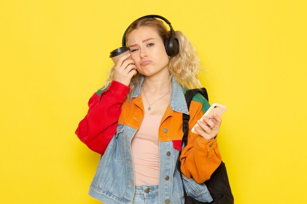 студентка молодая в современной одежде держит кофе и телефон на желтом