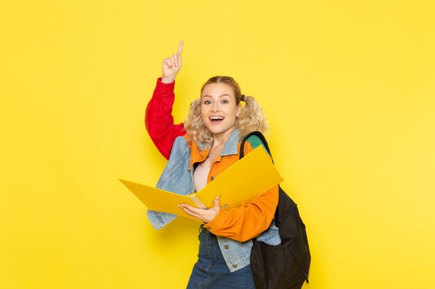 female student young in modern clothes holding files smiling on yellow