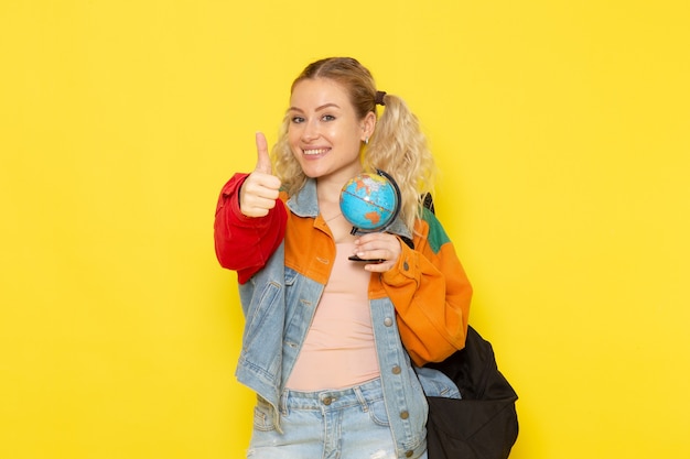 female student young in modern clothes holding a little globe and smiling on yellow