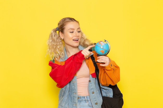 female student young in modern clothes holding little round globe on yellow
