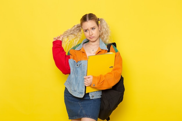 female student young in modern clothes holding yellow files and posing on yellow