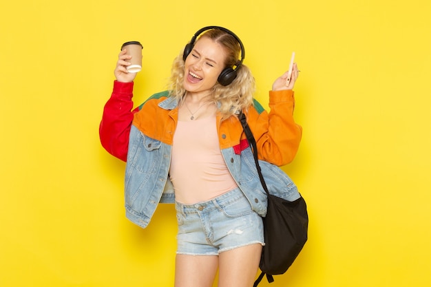 студентка молодая в современной одежде слушает музыку с кофе на желтом