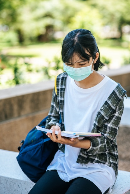 階段でマスクと本を身に着けている女子学生。