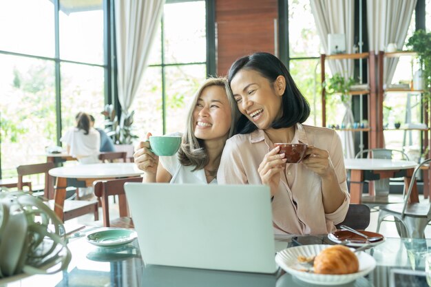 地元のコーヒーショップを勉強している女性。コーヒーを飲みながらカフェでビジネスプロジェクトについて話し合う2人の女性。スタートアップ、アイデア、ブレインストーミングのコンセプト。カフェでノートパソコンを使用して温かい飲み物で友達を笑顔