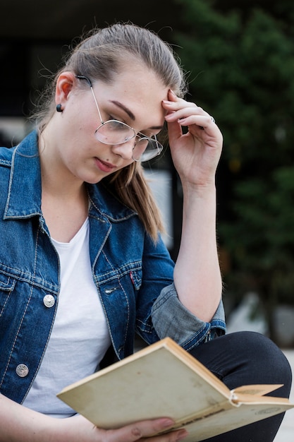 Foto gratuita femmina che studia con il libro che si siede nel parco