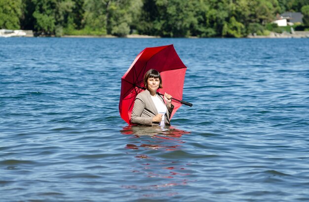 湖の真ん中に立っている赤い傘を持ってスーツを着た女性