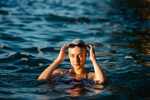 Female swimmer with cap and goggles posing while swimming in water