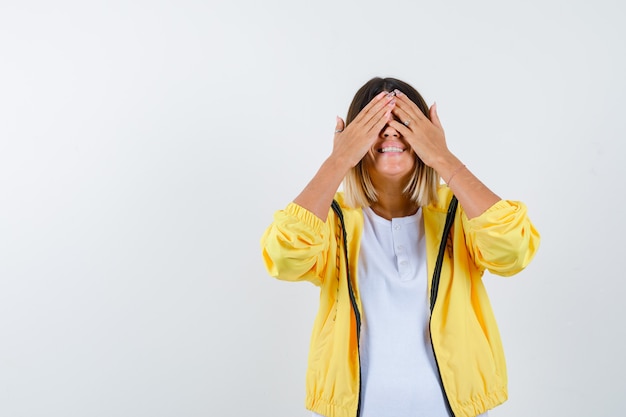 Female in t-shirt, jacket keeping hands on eyes and looking happy , front view.