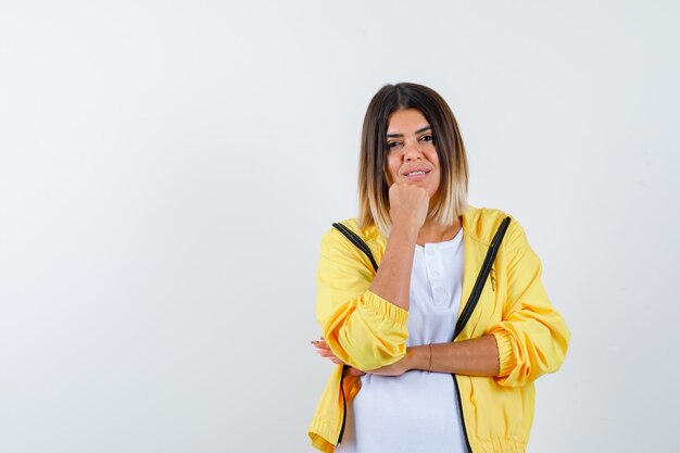 Female in t-shirt, jacket propping chin on fist and looking optimistic , front view.