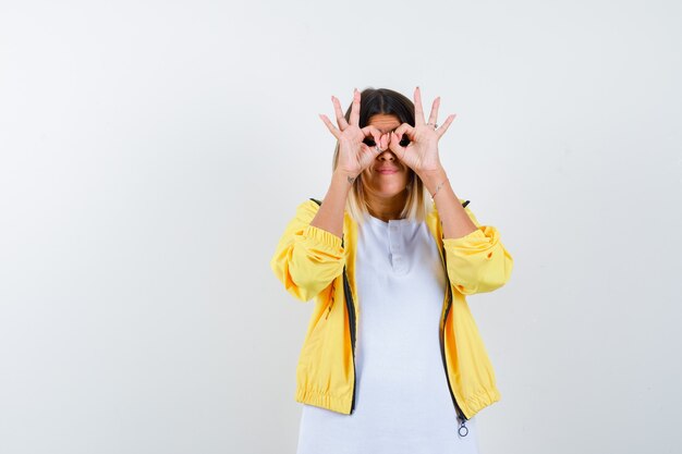 Female in t-shirt, jacket showing glasses gesture and looking focused , front view.