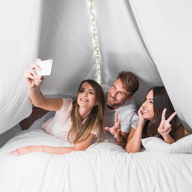 Selfie di presa femminile sul cellulare con i suoi amici che si trovano sul letto