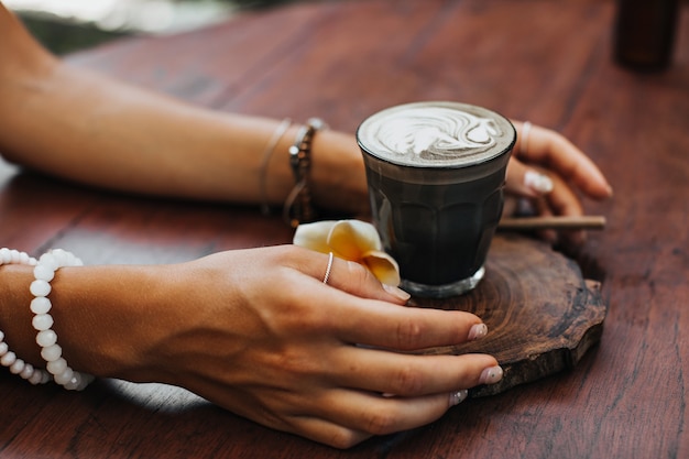 Female tanned hands holds glass of coffee with coconut milk