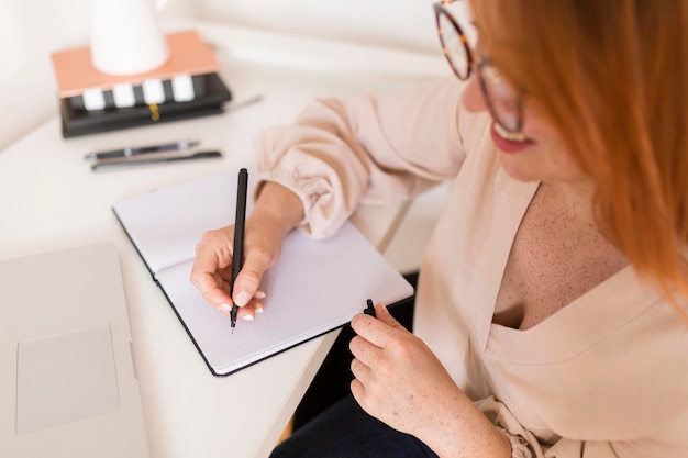 Female teacher at desk writing in agenda during online class