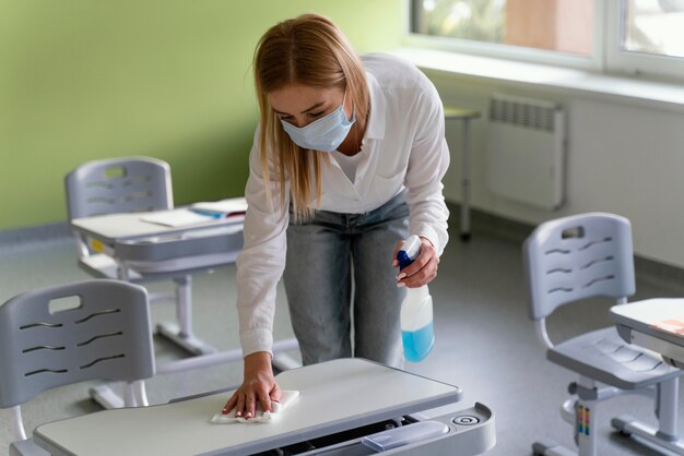 Female teacher disinfecting school benches in classroom