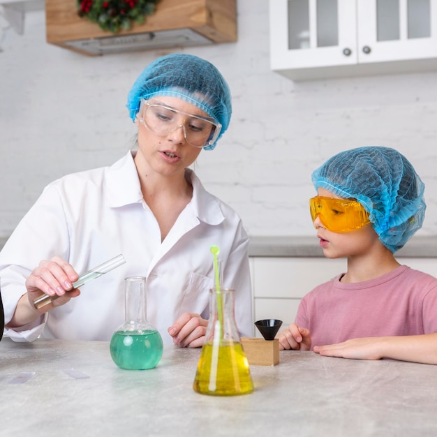 Insegnante femminile e ragazza con retine per capelli facendo esperimenti scientifici