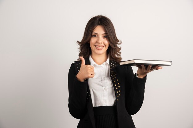 Female teacher giving thumbs up while holding a book.