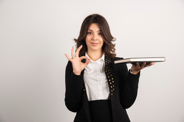 Female teacher making ok sign while holding a book.