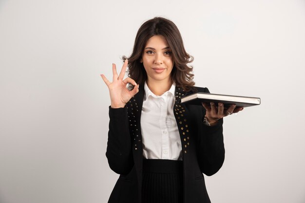 Female teacher making ok sign while holding a book.