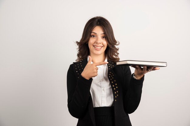 Female teacher pointing at book with happy expression.