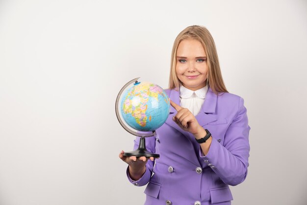 Female teacher pointing at globe on white.