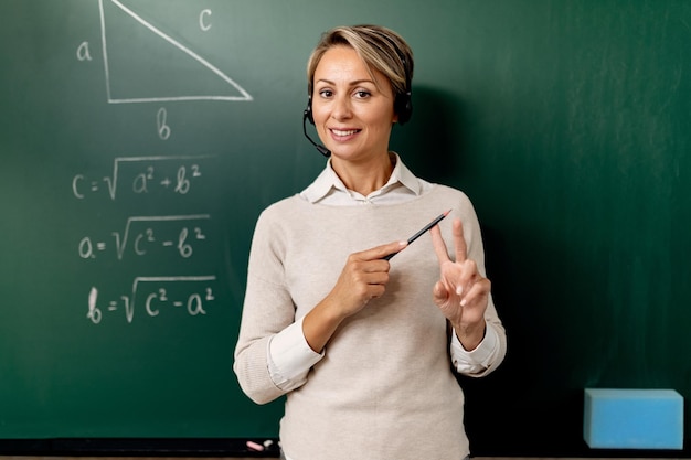 Female teacher standing in front of chalkboard and explaining mathematic during online class.