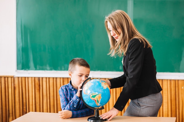 Female teacher and student boy working with globe