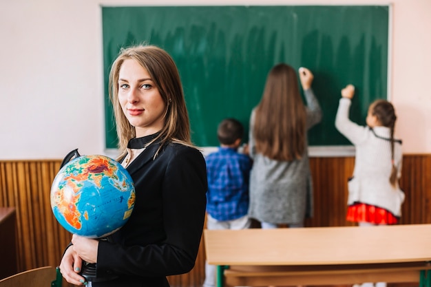 Female teacher with globe on classroom background