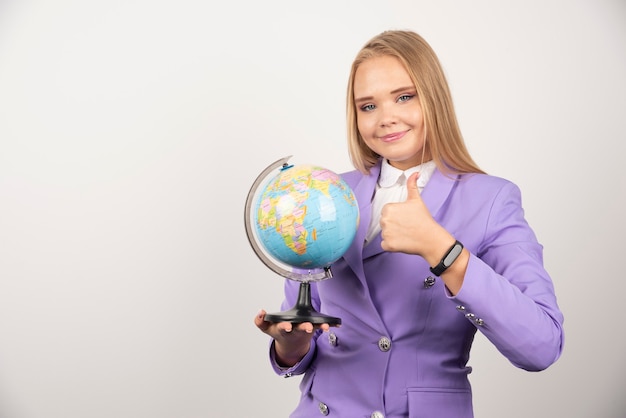 Female teacher with globe making thumbs up on white.