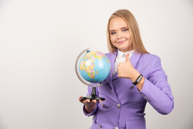 Female teacher with globe making thumbs up on white.