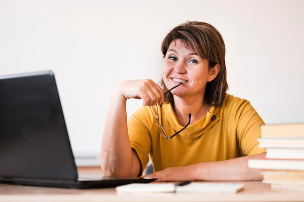 Foto gratuita insegnante femminile con il computer portatile che si siede allo scrittorio