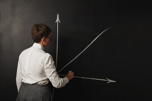 Female teacher with short hair in white blouse and grey skirt drawing a graph on blackboard