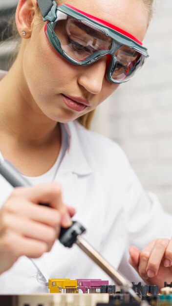 Female technician with soldering iron and safety glasses