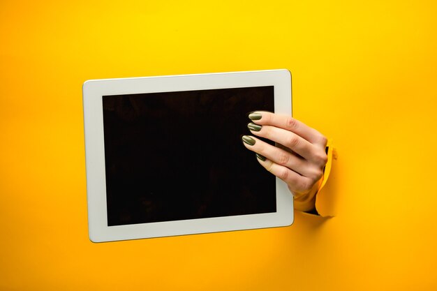 引き裂かれた黄色い紙を通して、孤立した、黒い画面でタブレットPCを使用して女性の十代の手