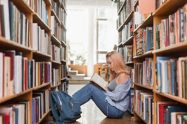 Женский подросток читает на пол библиотеки