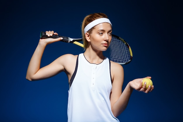  female tennis player with racket on shoulder and ball in hand posing 
