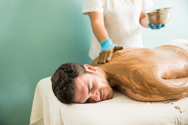 Female therapist giving a mud bath to a young man in a health spa