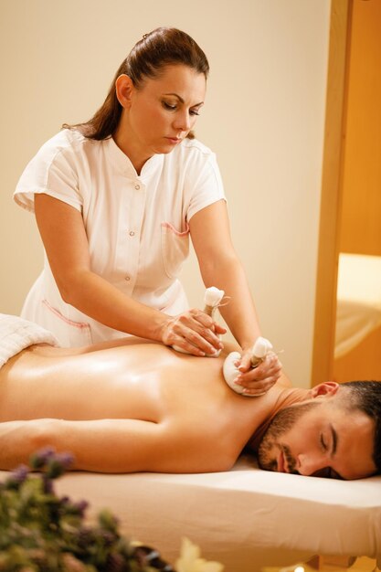 Female therapists massaging back of a man with Thai herbal compress at health spa