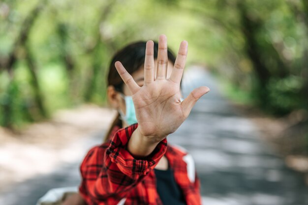 A female tourist carrying a backpack and raising her five fingers to ban on the road.