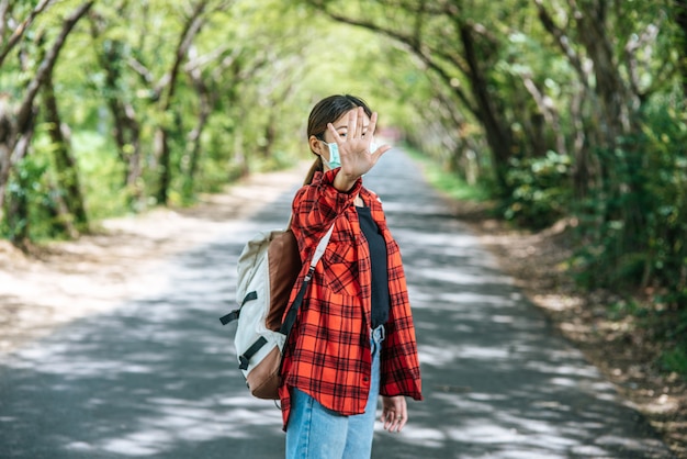 A female tourist carrying a backpack and raising her five fingers to ban on the road.