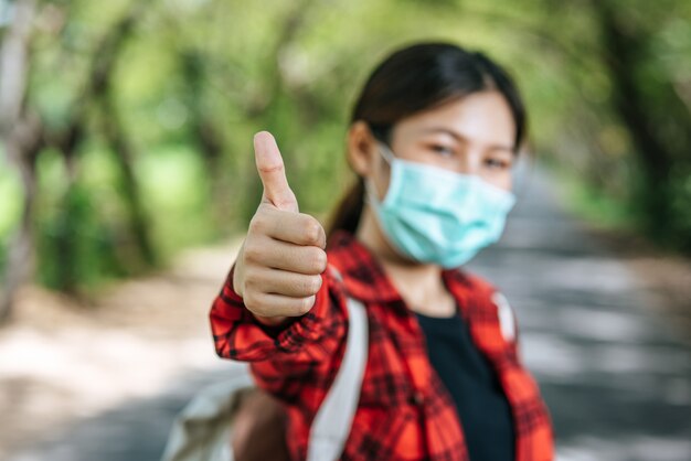 Female tourist carrying a backpack and thumbs up on the road.