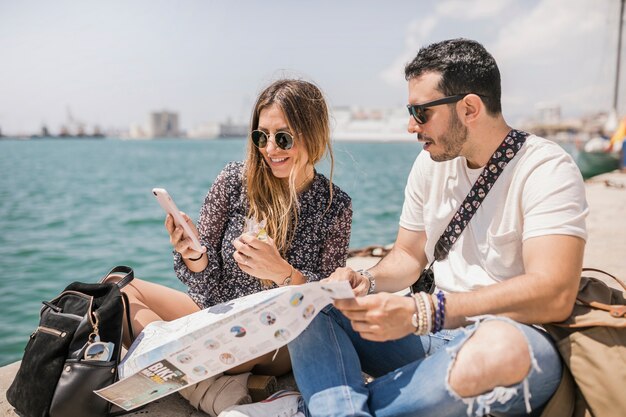 Female tourist showing her boyfriend cell phone sitting on jetty