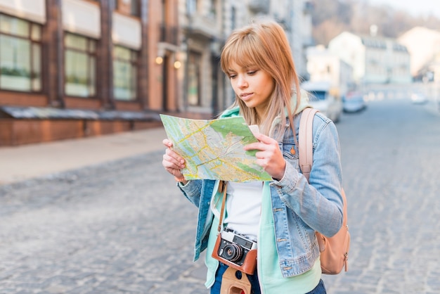 Female tourist standing on city street looking at map