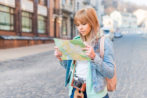 Female tourist standing on city street looking at map