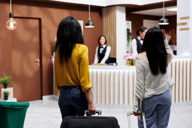 Foto gratuita turiste femminili che arrivano alla destinazione portando bagagli verso la reception di un resort moderno. turisti che iniziano la vacanza nella lobby di un hotel stravagante pronti a fare la prenotazione