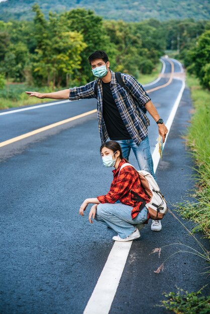 Female tourists sit, male tourists, pretend to hitchhiker Both wearing a mask and on the side of the road.