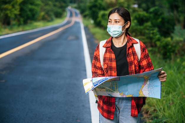 Female tourists stand and look at the map on the road.