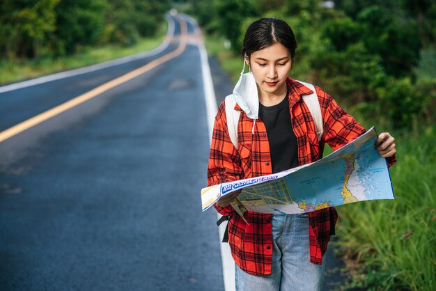 Female tourists stand and look at the map on the road.