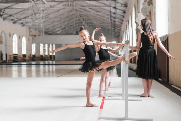 Женский тренер, глядя на девочек-балеринов, растягивая ногу на барре