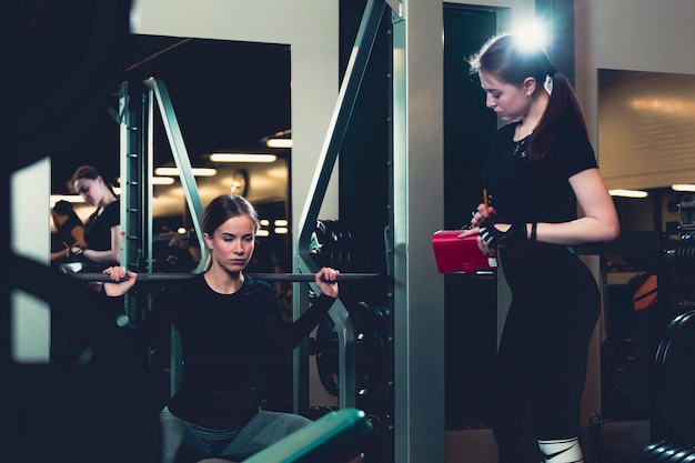 Female trainer looking at woman working out in gym