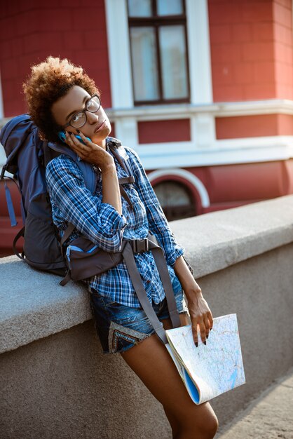 マップを保持しているバックパックを電話で話す女性旅行者。